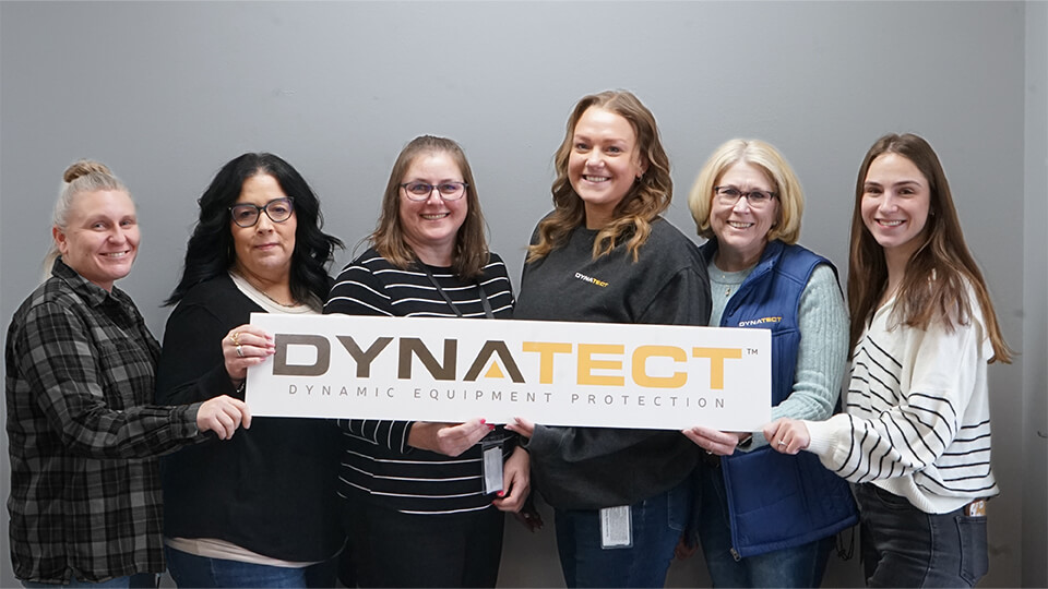 Human Resources holding a Dynatect sign in front of a gray wall.