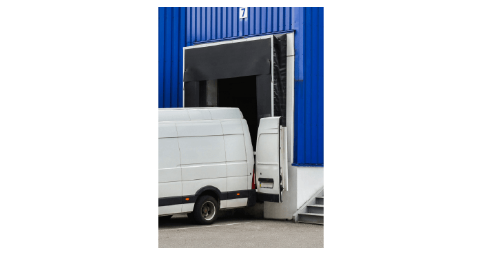 A white cargo van is backed into a loading dock with its roll-up door open. 